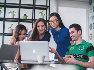 4 people standing around a computer screen. Used for a mindgenius blog promoting project management.